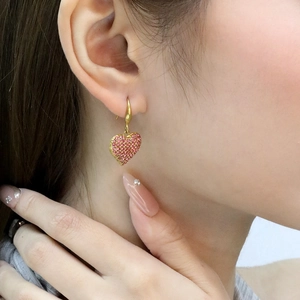 Détail de boucles d'oreilles cœur dorées avec cristaux roses portées sur un modèle
