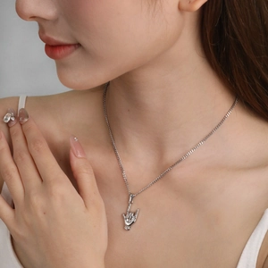 Détail macro du pendentif geste rock argenté sur une chaîne à mailles gourmette