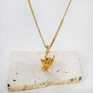 Collier minimaliste plaqué or avec pendentif geste rock sur présentoir en pierre