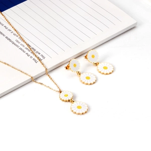 Close-up of golden daisy necklace and earrings set on a minimalist white notebook