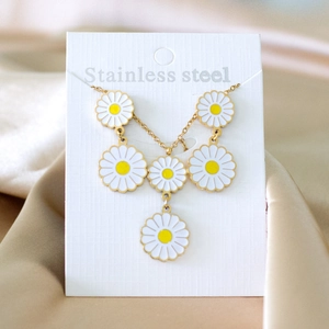 Golden stainless steel necklace featuring white and yellow daisy pendants on card