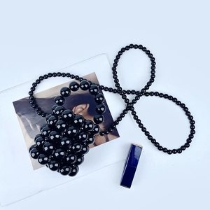 Detail of a black beaded mini bucket bag with glossy acrylic beads and crossbody strap