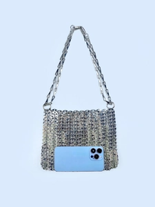 Detail of silver chainmail shoulder bag with metallic sequins next to a smartphone for scale