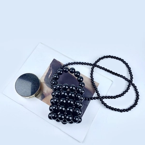 Close-up of black beaded mini bucket bag with glossy pearls and a matching strap