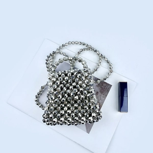 Detail of silver metallic beaded evening bag with crossbody chain next to a lipstick