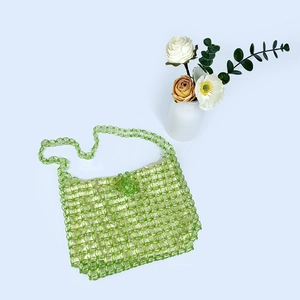 Detail of green handmade woven acrylic bead bag with decorative floral backdrop