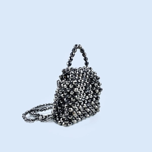 Detailed view of woven black beaded handbag with metallic facets and detachable chain strap