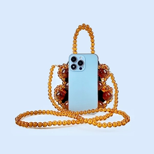 Detail view of mini amber beaded bucket bag with smartphone to demonstrate size capacity