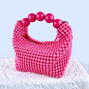 Detail of pink beaded handbag with large decorative sphere handle on white knit