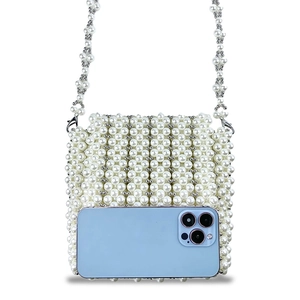 Détail d'un sac à bandoulière en perles blanches montrant sa taille face à un smartphone