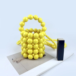 Mini yellow beaded bucket bag with shoulder strap next to a blue lipstick for scale