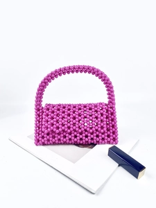 Detailed view of handcrafted purple beaded handbag with a glossy resin finish on a white book
