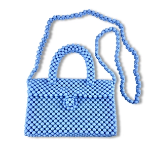 Close-up of light blue beaded handbag with circular handle and matching woven chain strap
