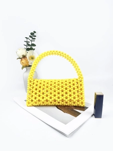 Detail of a bright yellow handcrafted beaded handbag with a large handle on a white stand
