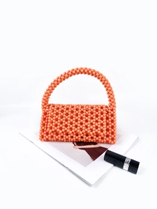 Detail of orange handmade beaded handbag with Dior lipstick on fashion magazine