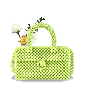 Detailed view of light green hand-beaded handbag with floral accents and woven texture