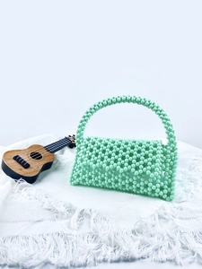 Close-up of a handmade light green beaded handbag on a cozy white knit blanket