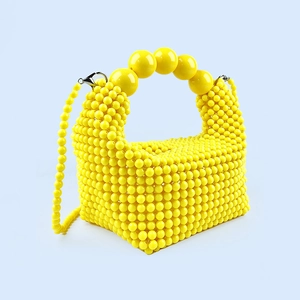 Detailed close-up of handmade yellow beaded handbag with round pearl handle and silver clips