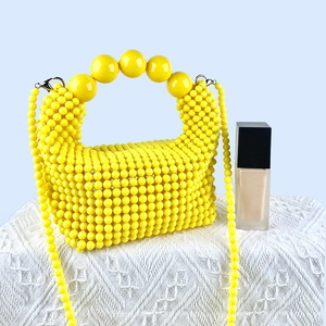Detail of yellow beaded handbag featuring large round beads on handle and pearl-like strap