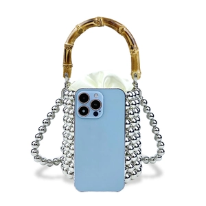 Silberne Perlen-Eimertasche mit Bambusgriff und Kordelzug-Futter neben einem Smartphone