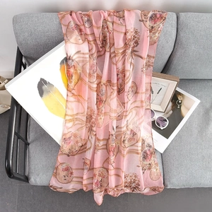 Pink floral chiffon scarf with gold prints on grey sofa in cozy home setting