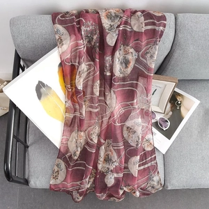 Burgundy printed scarf with gold pattern and stripes on a grey fabric background