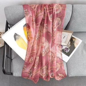 Light pink lightweight floral scarf with gold foil printing on grey sofa