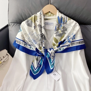 Elegant 90x90cm floral twill silk scarf with blue trim hung on a wooden hanger