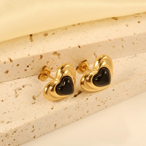 Polished gold heart studs with black inlay on a beige stone and silk background