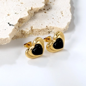 Detail of heart stud earrings featuring gold plating and black enamel on a stone surface