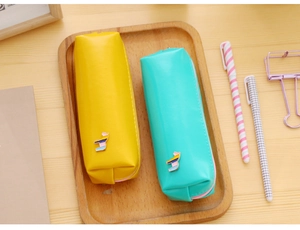 Detail of yellow and green PU leather pencil cases with cute pony charms on a wooden tray