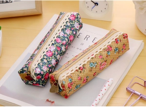 Detail of floral canvas pencil cases with lace trim and vintage metal zippers on wood desk