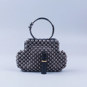 Detail of dark grey beaded shell bag with metal ring handle and lipstick size reference