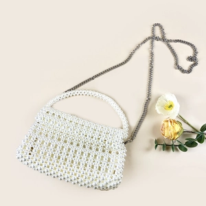 Gros plan d'un sac à main en perles blanches avec chaîne métallique et fleurs élégantes