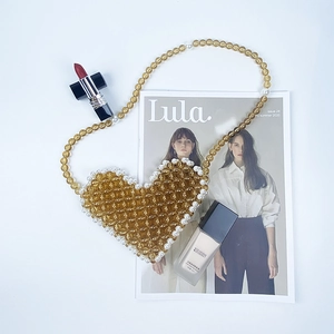 Detailed view of a handmade amber beaded heart-shaped crossbody bag on a fashion magazine