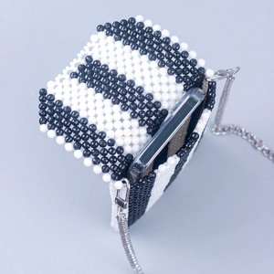Macro view of a handmade black and white striped beaded crossbody bag holding a smartphone
