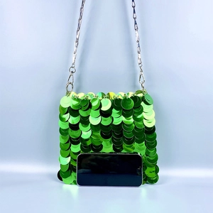 Close-up of emerald green sequin shoulder bag with silver chain and smartphone for size