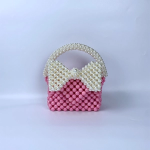 Detail van roze handgemaakte kralenhandtas met een grote witte decoratieve parelstrik