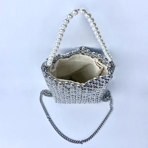 Close-up of woven silver beaded handbag with large white faux pearl handle and metal chain