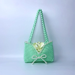 Detail of mint green beaded handbag featuring white pearl bow accent and satin lining