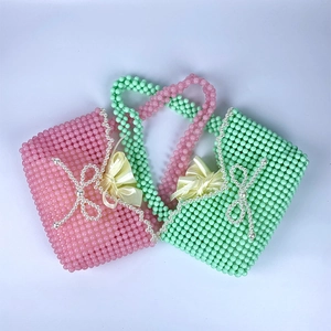 Detail of handmade beaded pearl handbags in pink and mint green with satin bow accents