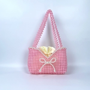 Detailed shot of pink beaded handbag featuring a white pearl bow and satin drawstring liner