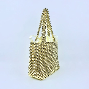 Detail of handmade gold beaded handbag featuring woven pearls and a satin drawstring liner