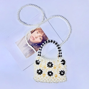 Detail of handmade beaded pearl handbag featuring black floral accents and a pearl strap
