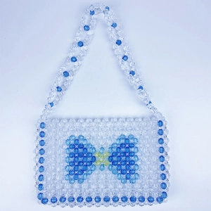 Detail view of a handmade beaded handbag featuring a blue bow pattern and woven handles