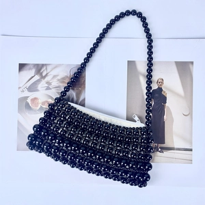 Close-up of black beaded handbag with pearl chain handle and white zipper detail