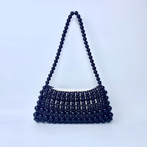 Close-up of a handmade black beaded baguette bag with a structured pearl chain strap