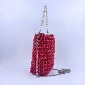 Detail of red beaded bucket bag featuring white pearl handle and silver metal chain strap