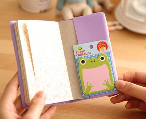 Close-up of cute green frog sticky notes and purple stationery set on wooden desk