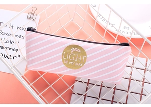 Detail of pink striped canvas pencil case with golden quote badge in white metal basket